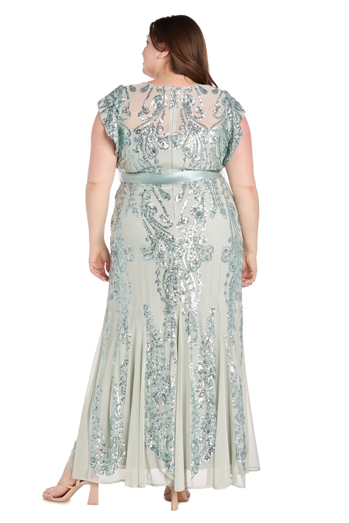 A woman stands with her arms relaxed at her sides, shown from the back in the Plus-Size Sage Green Formal Dress: R&M Richards 3465W—a light, floor-length gown with silver sequin embellishments for an elegant look.